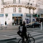 A cyclist pauses at a zebra crossing in front of a pharmacy in Paris, capturing urban life.